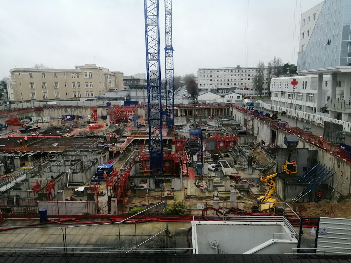 Construction workers operate machinery at a busy urban building site.
